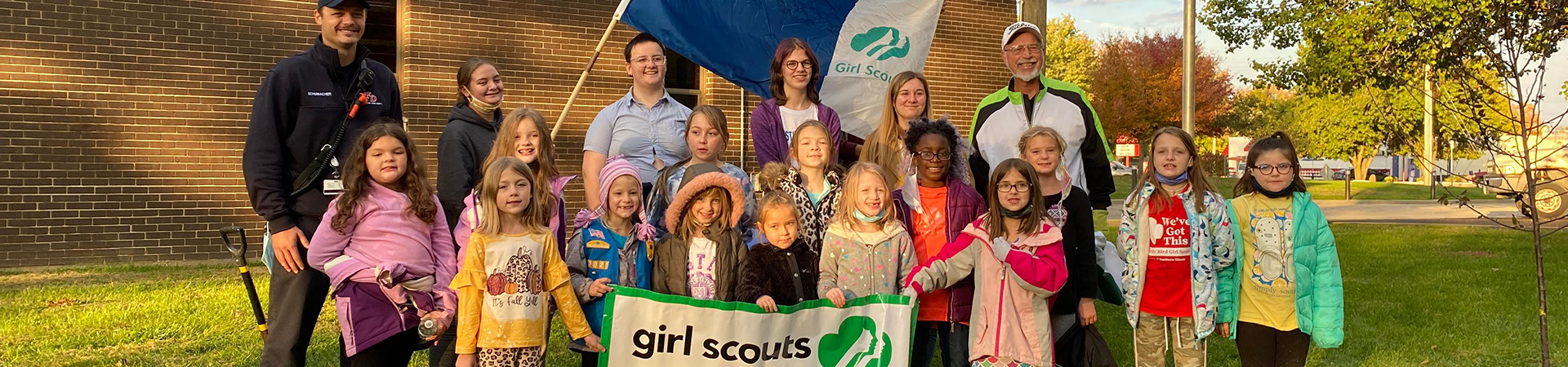  girl scout service unit taking a group photo with girl scout flags outside 